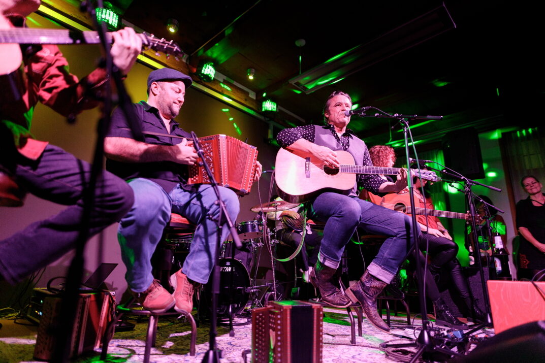 Musiker mit Akkordeon und Gitarren im Kreis auf der Bühne