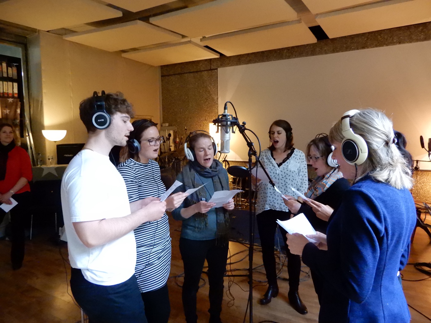 Teammitglieder mit Kopfhörern singen im Studio am Mikrofon